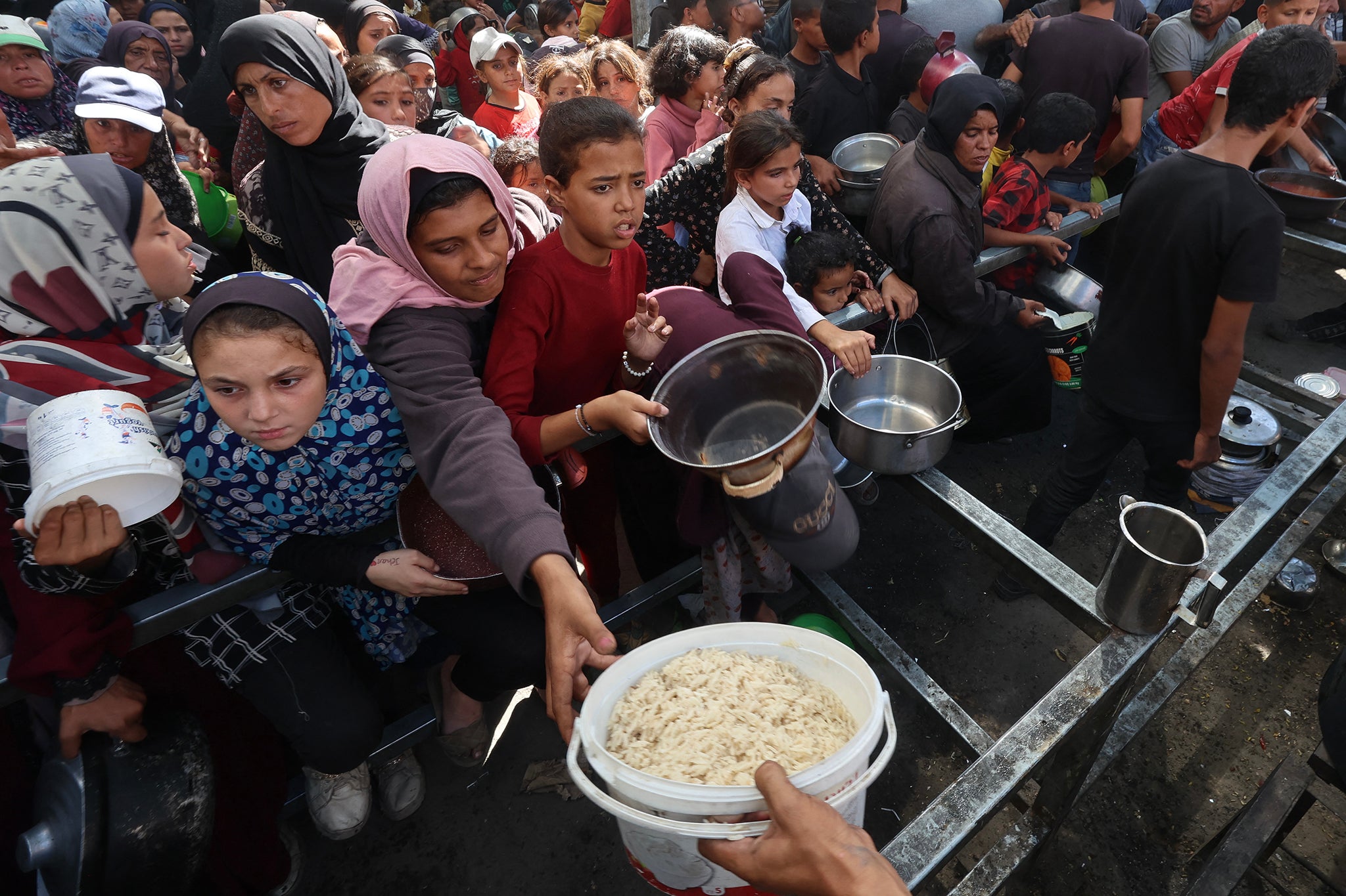 Palestinians gather to receive food from a charity kitchen in the Nuseirat refugee camp in the central Gaza Strip, on 15 October 2025, two days after a ceasefire came into effect