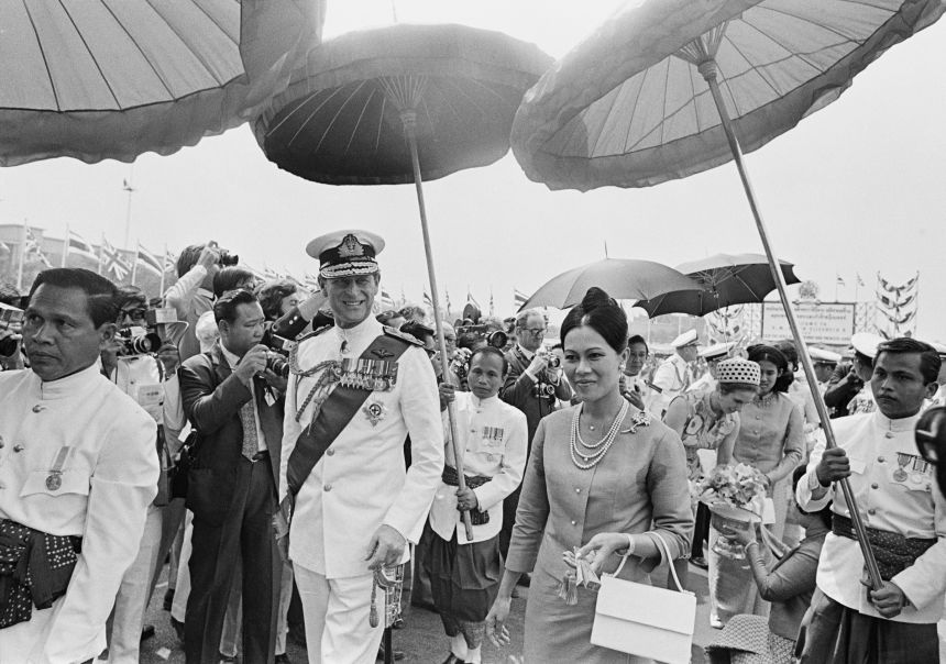 Prince Philip walking with Queen Sirikit during the royal tour of Thailand, February 16th 1972. Princess Anne can be seen receiving a gift in the background.