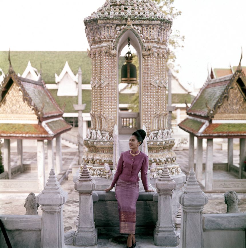 Queen Sirikit of Thailand, standing before a porcelain encrusted tower in one of the many pavilions of the Grand Palace